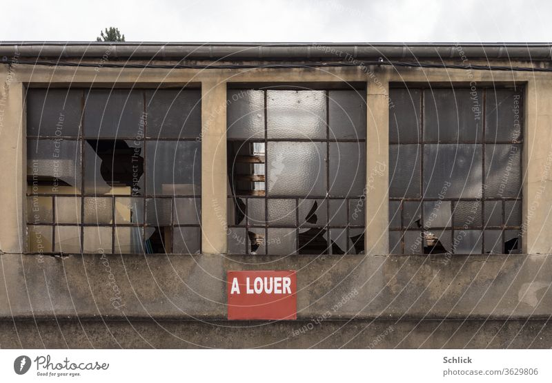 Fassade eines maroden Industriegebäudes mit zerstörten Fenstern und rotem Schild a louer zu vermieten kaputt text Himmel Baumwipfel Hoffnung Buchstaben Wort