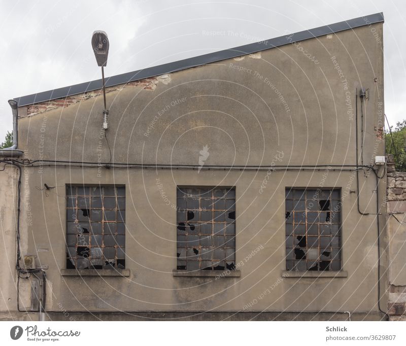 Alte Fassade einer Fabrikhalle mit geborstenen Fenstern und Außenbeleuchtung Industrie alt kaputt geringe Farbsättigung blasse Farben Wand Glas Eisen Kabel grau