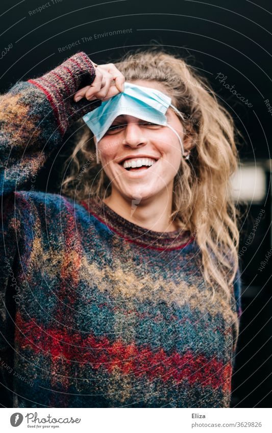 Junge Frau macht Quatsch mit einem medizinischem Mundschutz Maske MNS lachen Corona Schutz falsch Alternativ Augen anfassen ironisch Spaß Quatsch machen