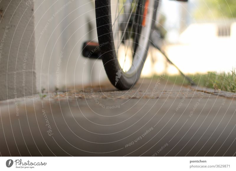Ein Fahrrad steht vor einem Haus. Blick von unten. Teilansicht. Reifen, Pedal, Fahrradständer reifen abgestellt mobilität sommer sonnenlicht parken