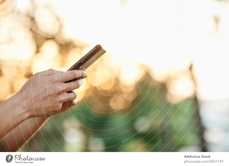 Anonyme Frau mit Smartphone im Park stehend benutzend genießen Browsen jung trendy Lifestyle Apparatur Gerät Kälte positiv soziale Netzwerke Lächeln online