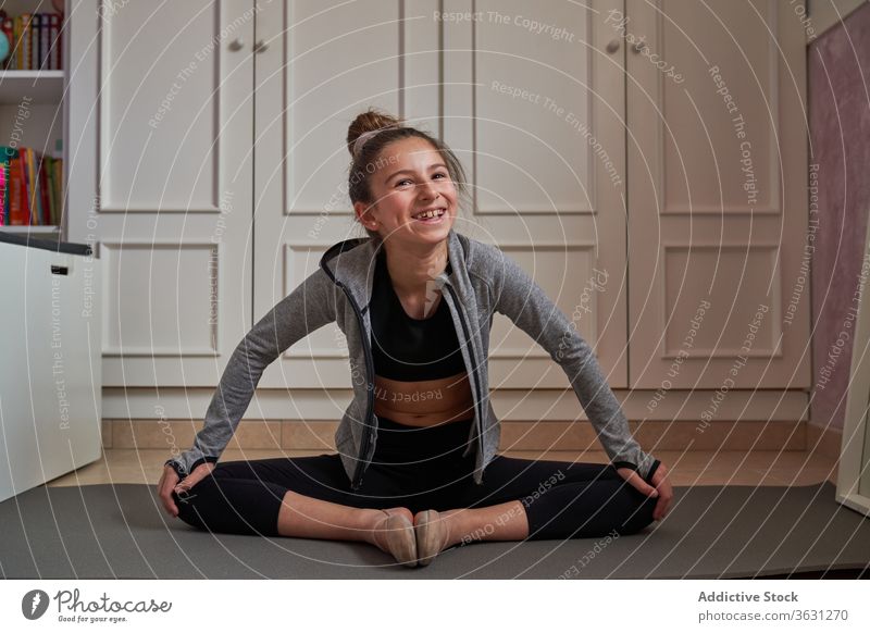 Fröhliches Mädchen sitzt in Lotus-Pose und streckt sich gymnastisch Lachen Dehnung Unterlage heimwärts Kind Künstler Glück Zeitgenosse Körperhaltung Training