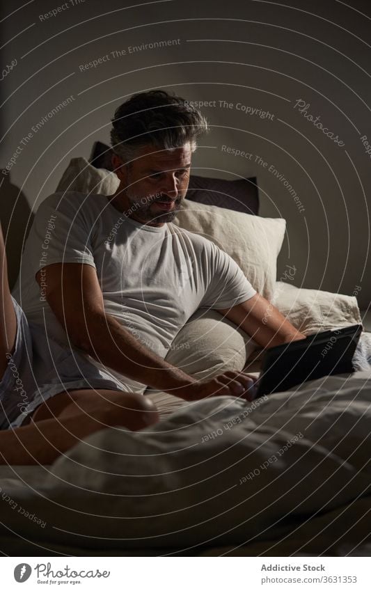 Mann benutzt Laptop im Schlafzimmer heimwärts Bett Browsen benutzend positiv Lächeln reif Lügen ruhen männlich lässig Gerät Apparatur sich[Akk] entspannen