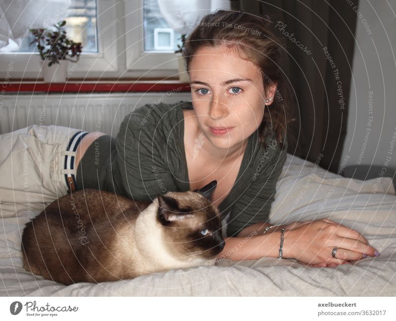 junge Frau liegt zuhause mit Katze auf Bett Junge Frau Siamkatze Haustier liegen hübsch lächeln entspannen zimmer tierlieb Schlafzimmer Tier Erholung Tag