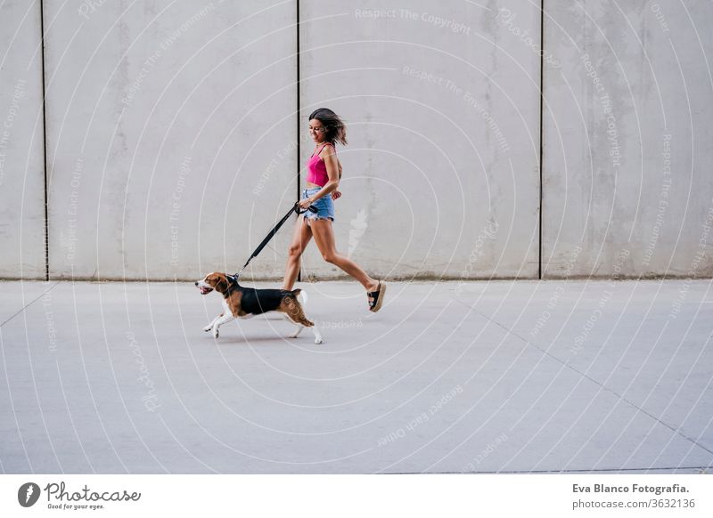 glückliche junge Frau, die mit einem Beagle-Hund im Freien spazieren geht. Familien- und Lebensstilkonzept Großstadt urban Lifestyle laufen Freizeitkleidung