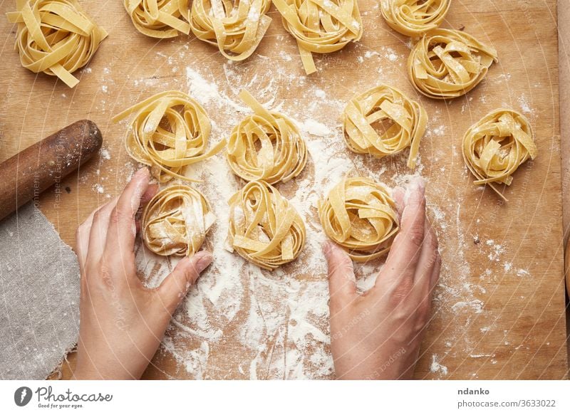 rohe Fettuccine Pasta und zwei Frauenhände kochen Pasta Spätzle Vorbereitung vorbereitend gerollt rund Spaghetti Tisch traditionell ungekocht Vegetarier Weizen