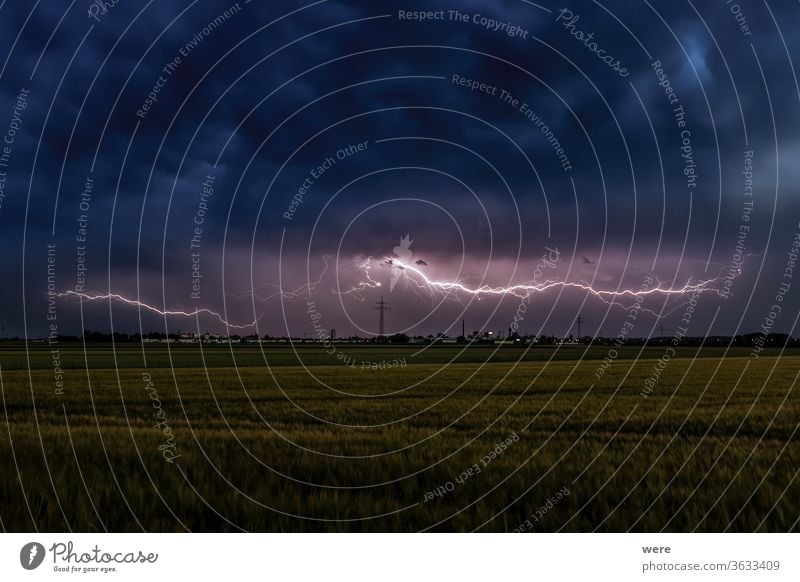Gewitterstimmung mit Blitzen über Weizenfeldern bei bewölktem Himmel und Blick auf Inningen bei Augsburg Ansicht Atmosphäre bewölkter Himmel Textfreiraum dunkel