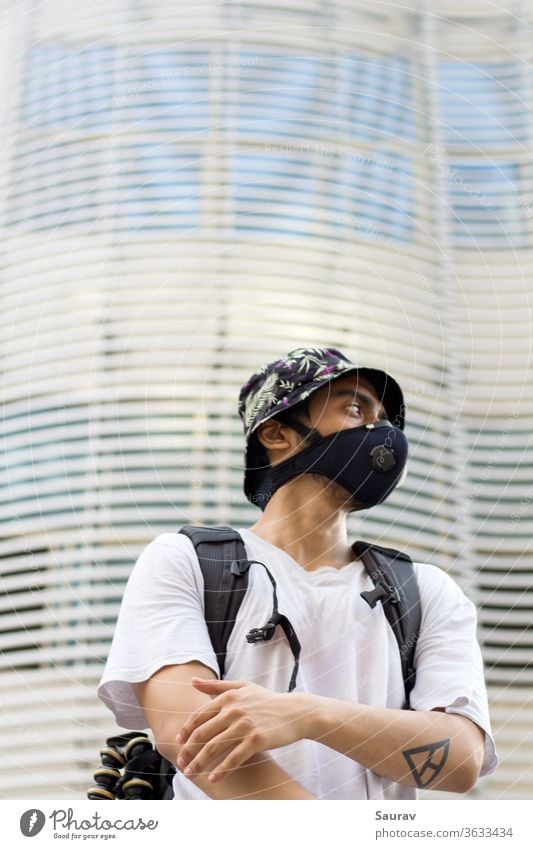 Ein junger Mann im Freien mit einer schützenden Gesichtsmaske zum Schutz vor einer Infektion mit dem Coronavirus, der während einer globalen Pandemie eine mit Blumen bedruckte Eimerkappe und einen Beutelpack trägt.
