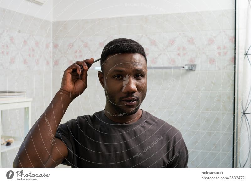 Junger schwarzer Mann kämmt Haare und schaut in die Kamera Kamm Kämmen Behaarung Gesicht Frisur 1 Mensch afrikanische ethnische Zugehörigkeit Lifestyle