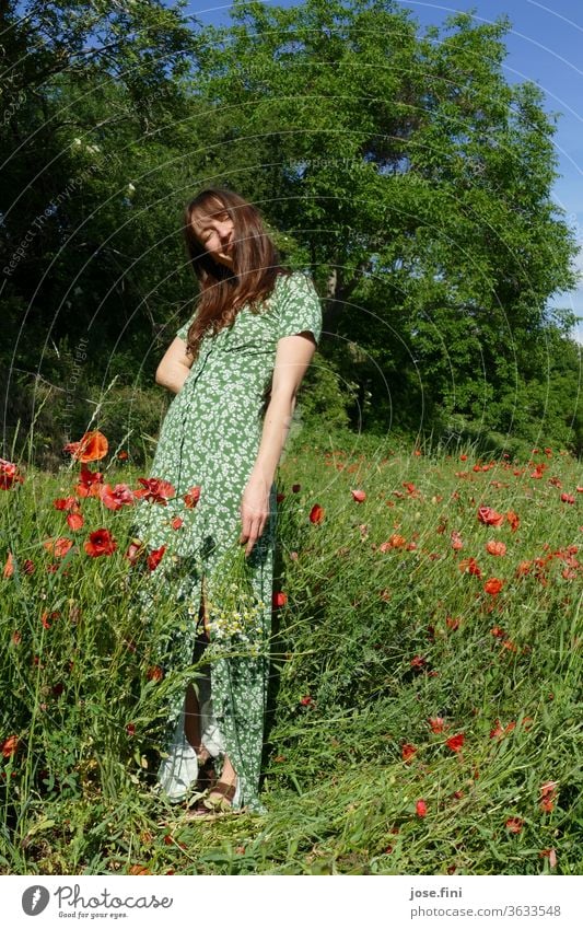 Frau steht im langen Sommerkleid im Mohnfeld mit einem Blumenstrauß in der Hand und lächelt verschmitzt. Kleid romantisch ruhig träumen Farbfoto Stimmung posen
