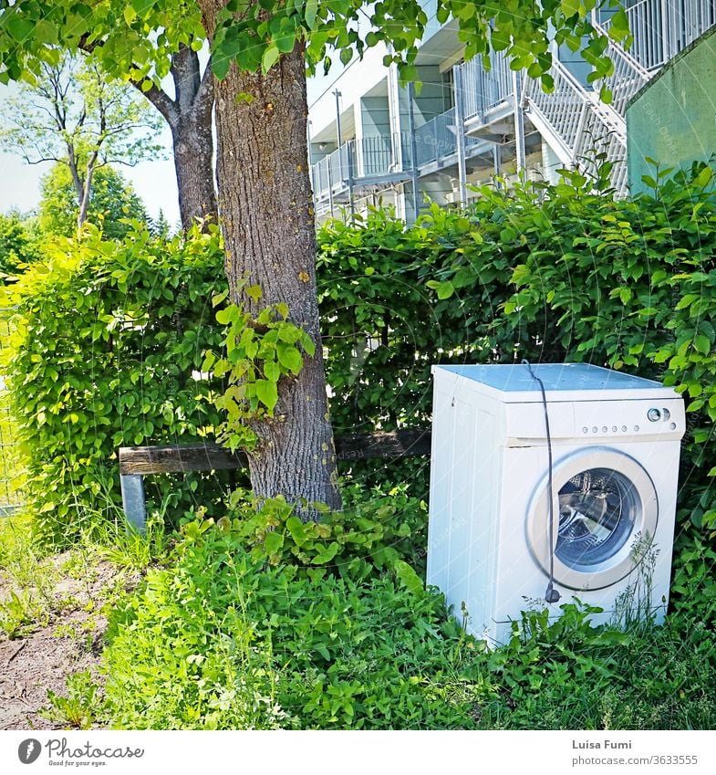 Eine Waschmaschine, die als Müll deponiert und auf dem Bürgersteig zurückgelassen wurde, in scharfem Kontrast zur grünen Umgebung abgeladen Verlassen abgeworfen