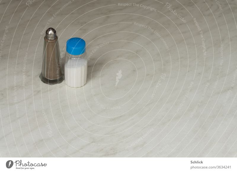 Salz und Pfeffer stehen einsam auf einer weißen Marmorplatte Salzstreuer Pfefferstreuer Tisch viel textfreiraum Kunststoff Glas Metall verschieden