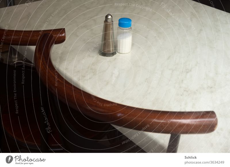Salz und Pfeffer stehen einsam auf einem weißen Marmortisch zwei Stühle sind an den Tisch geschoben Salzstreuer Pfefferstreuer Marmorplatte viel textfreiraum