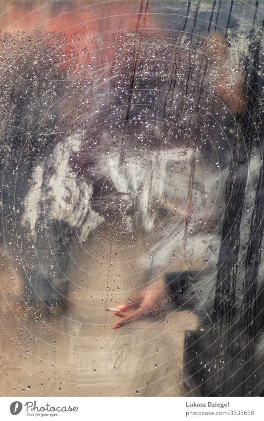 Hand mit Zigarette im Fenster voller Regentropfen am Regentag Straße Zigarettenrauchen verschwommen Tröpfchen Wetter Form Kondenswasser urban Textur Rauch