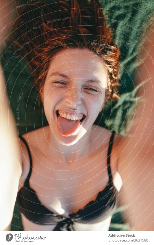 Fröhliche Frau im Bikini mit Zunge Zunge zeigen Grimasse expressiv Gesicht machen Sommer Sonnenbad Bräune heiter Urlaub Lügen Strand sonnig sich[Akk] entspannen