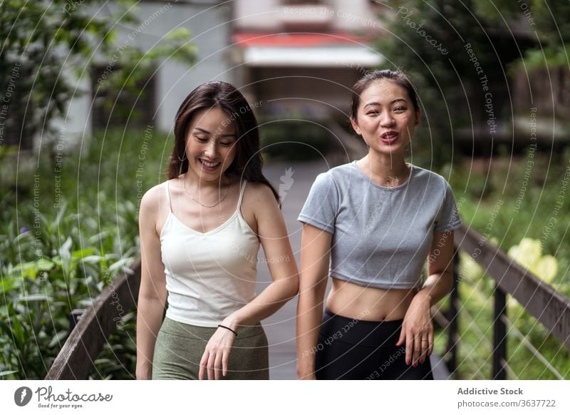 Positive junge ethnische Frauen, die über eine schmale Brücke auf dem Land gehen Freundin Spaziergang positiv Talkrunde Zahnfarbenes Lächeln lässig passen