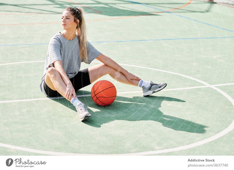 Basketballspielerin auf dem Sportplatz sitzend Frau Übung Aufwärmen Sportpark Training vorbereiten Spieler Ball Gericht Aktivität Lifestyle Wohlbefinden jung