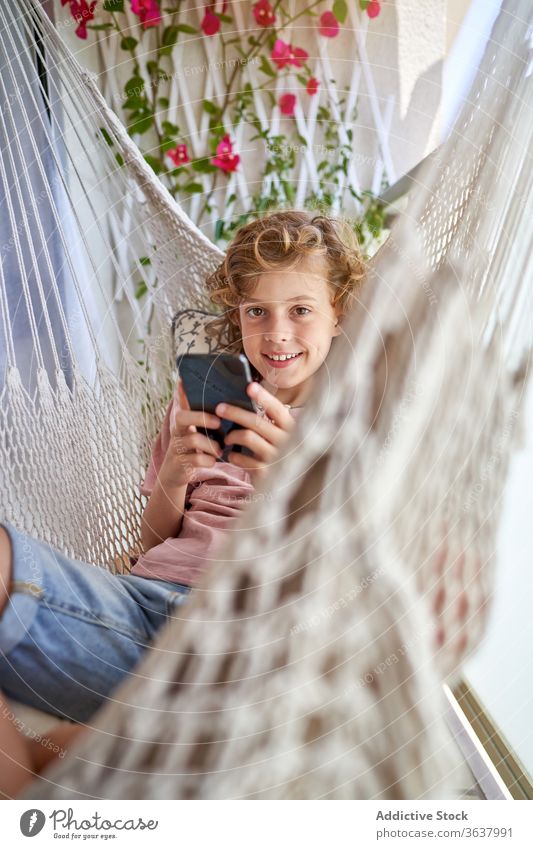 Junge nimmt Selfie auf Smartphone sitzend in Hängematte Wochenende Kindheit Zahnfarbenes Lächeln Komfort ruhen benutzend Apparatur Gerät Funktelefon Harmonie