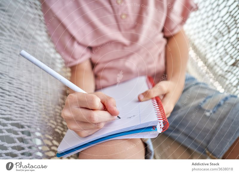 Anonymer Schuljunge mit Brille lernt in Hängematte mit Heft zu Hause lernen Bildung Hausaufgabe Wissen intelligent fokussiert Schönschreibheft Bleistift Junge