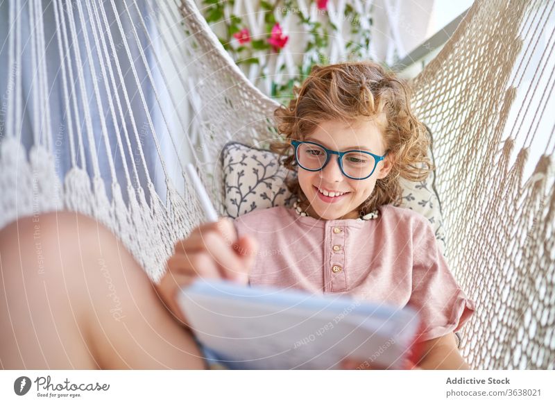 Brillenschüler lernt in Hängematte mit Heft zu Hause Schuljunge lernen Bildung Hausaufgabe Wissen intelligent fokussiert Schönschreibheft Bleistift Junge