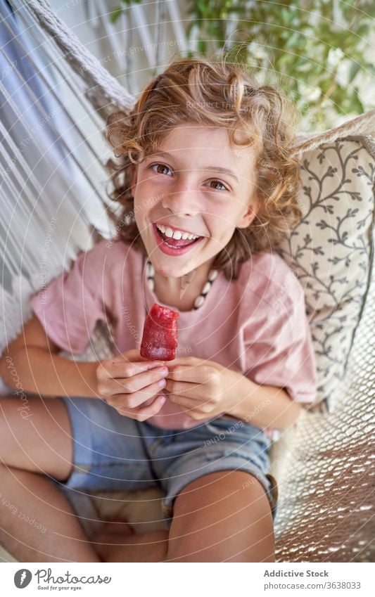Zufriedener Junge genießt köstlichen Fruchteis-Lolly in der Hängematte sitzend Eis Kies essen Kind lecker Wochenende Beine gekreuzt Barfuß Mund geöffnet