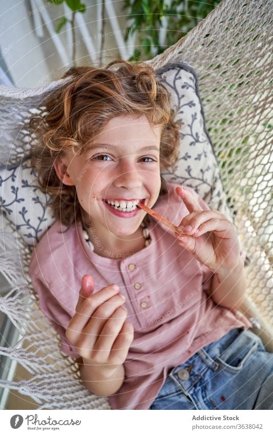 Zufriedener Junge genießt köstlichen Fruchteis-Lolly in der Hängematte sitzend Eis Kies essen Kind lecker Wochenende Beine gekreuzt Barfuß Mund geöffnet