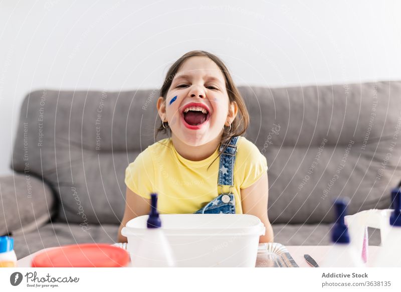 Ausdrucksstarkes Mädchen mit schmutzigen Fingern sitzt zu Hause auf dem Sofa Grimasse expressiv Mund geöffnet spielerisch diy kreativ spielen heimisch Kind