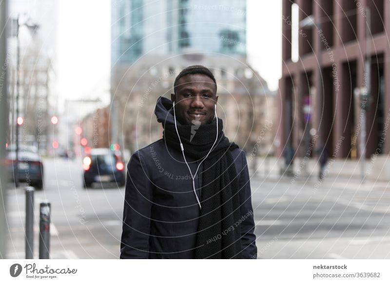 Hübscher schwarzer Mann mit Kopfhörern posiert auf der Straße der Großstadt Porträt afrikanische ethnische Zugehörigkeit Lächeln Mantel Herbst hören Musik