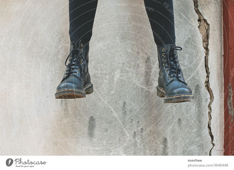 baumelnde füße einer teenagerin, die auf einer mauer sitzt | symmetrie Beine Füße Schuhe Stiefel cool sitzen Jugendliche Mauer Mauerriss Außenaufnahme