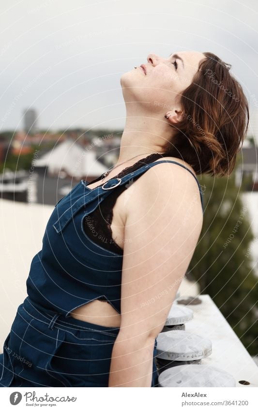 Portrait einer jungen, sommersprossigen Frau auf einem Dach die in den Himmel schaut junge Frau Top windig Haare brünett schön intensiv Jugendliche 18-25 Jahre