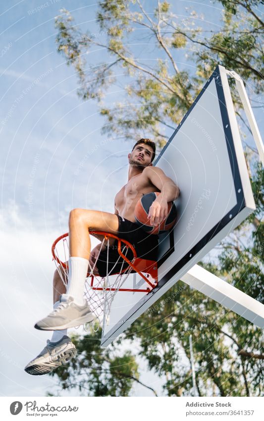 Basketballspieler sitzt auf einem Korb auf dem Spielplatz Reifen Mann Sportler Spieler Training Ball Gesundheit männlich gutaussehend professionell Aktivität
