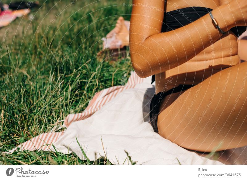 Junge Frau im Bikini auf einer Decke in der Wiese bei Sonnenschein. Badewetter sonnen Sommer Natur sitzen Erholung sommerlich draußen Liegewiese