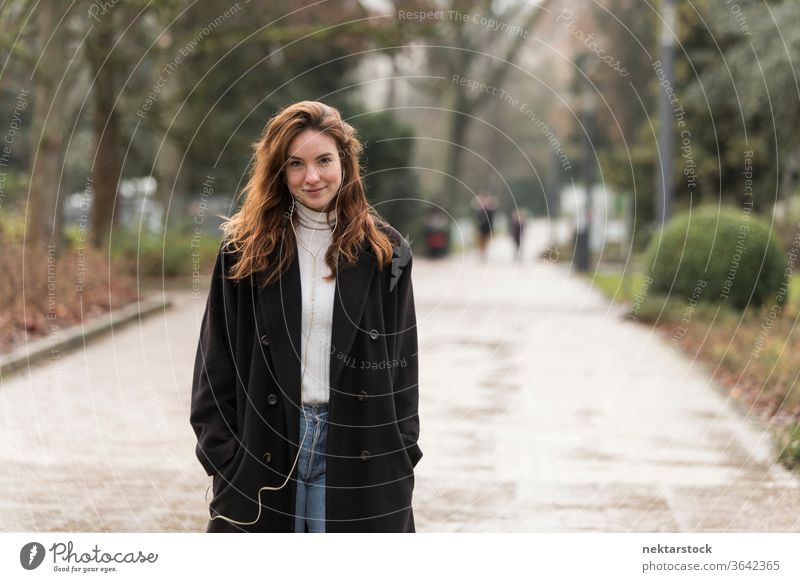 Schöne junge Frau lächelt auf der öffentlichen Straße im Park kaukasische Ethnizität Kopfhörer Audio Musik hören braune Haare Modell aus dem wirklichen Leben