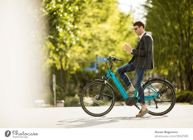 Junger Geschäftsmann auf dem E-Bike mit dem Handy Erwachsener Fahrrad Business Kaukasier Großstadt Pendler Fahrradfahren Radfahrer Tag ebike Öko ökologisch