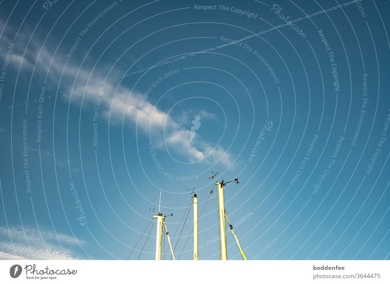 Spitzen von drei weißen Segelmasten mit Funkortungs- und Radaranlagen gegen blauen Himmel mit Federwolke und Kondensstreifen, die sich beide kreuzen