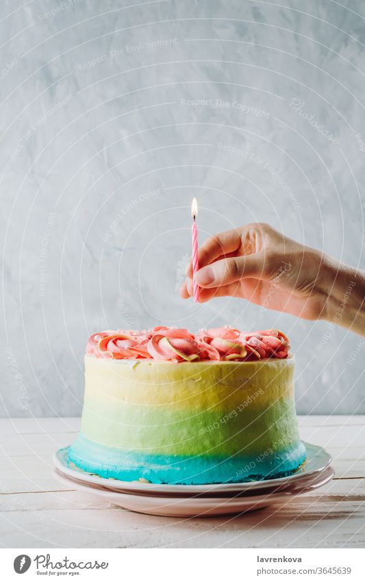 Nahaufnahme eines bunten veganen Kuchens und der Hand einer Frau, die darüber eine Geburtstagskerze hält, selektiver Fokus Finger Hände Kerze Beteiligung