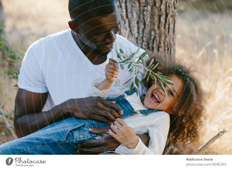 Glücklicher afroamerikanischer Vater umarmt Tochter in der Natur Baum Mulatte schwarz Umarmung Runde ruhen bezaubernd Sommer positiv Wald Lächeln lässig