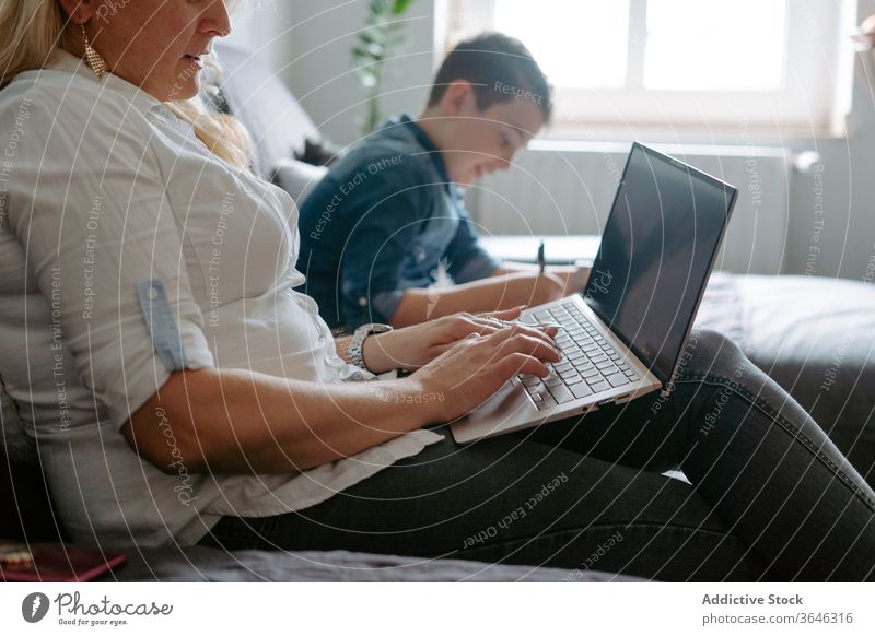 Positive Mutter und Sohn ruhen mit Laptop auf dem Sofa benutzend modern Inhalt Glück Lächeln Glas heiter lernen Schot sich[Akk] entspannen Papier Browsen Eltern