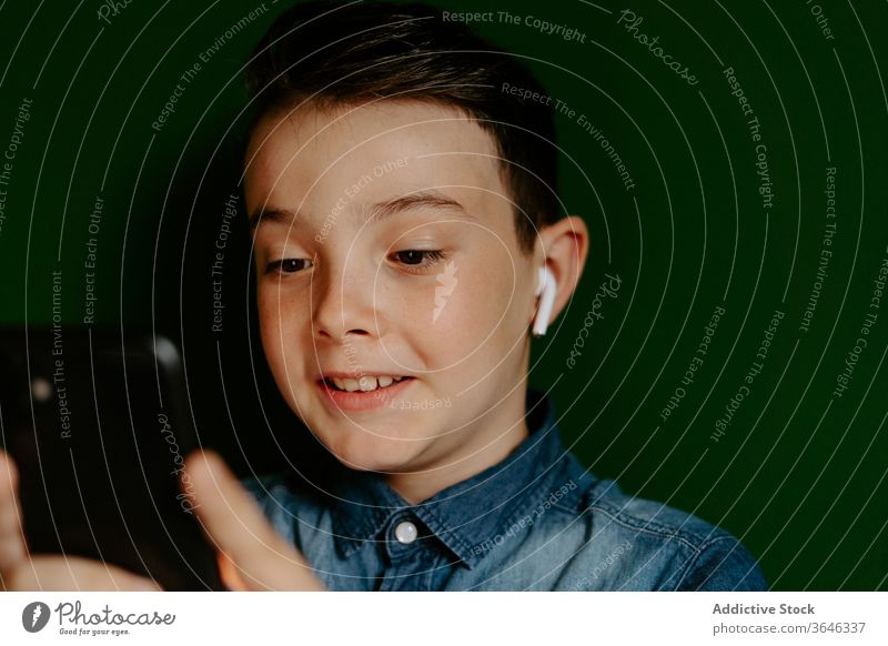 Zufriedener Junge in Ohrstöpseln mit Smartphone benutzend zuhören Musik Inhalt positiv Apparatur Drahtlos modern Favorit Mobile Telefon Surfen soziale Netzwerke