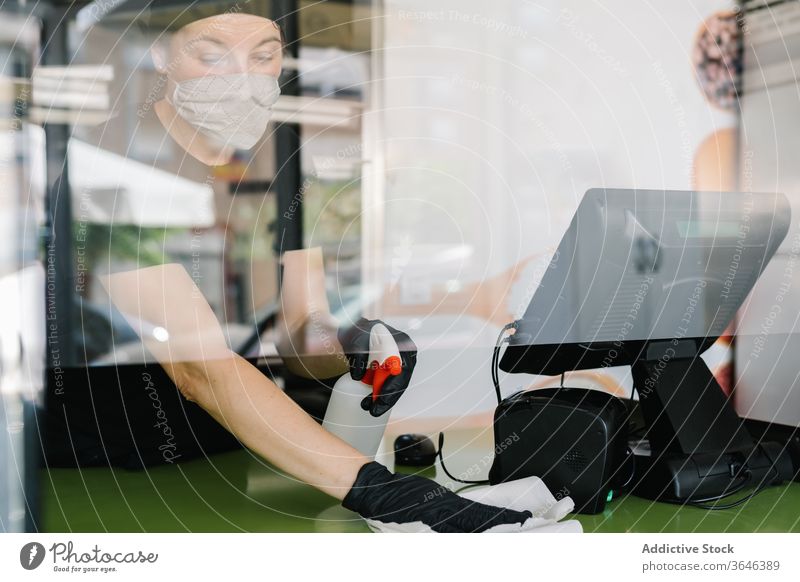 Weibliche Kassiererin in Gesichtsmaske wischt mit einem Tuch die Theke Frau Wischen Atemschutzgerät Abfertigungsschalter Café Handschuh Coronavirus
