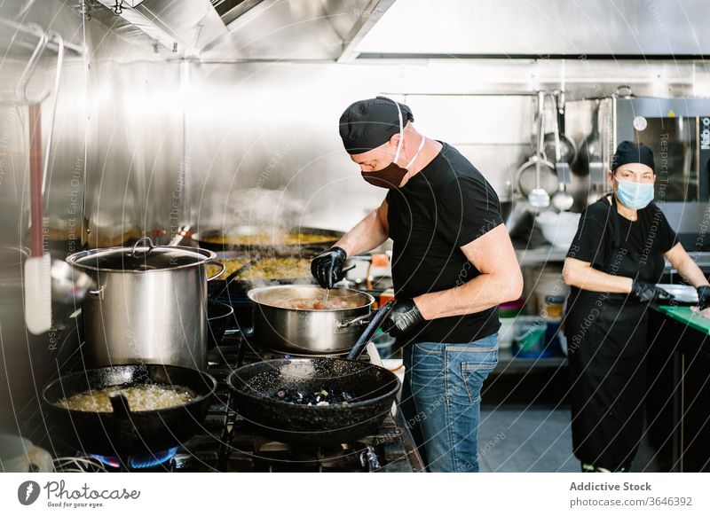 Fokussierter männlicher Koch in Gesichtsmaske Koch bereitet Mahlzeit zu Küchenchef Frau Atemschutzgerät ernst Restaurant Coronavirus Bestandteil Lebensmittel