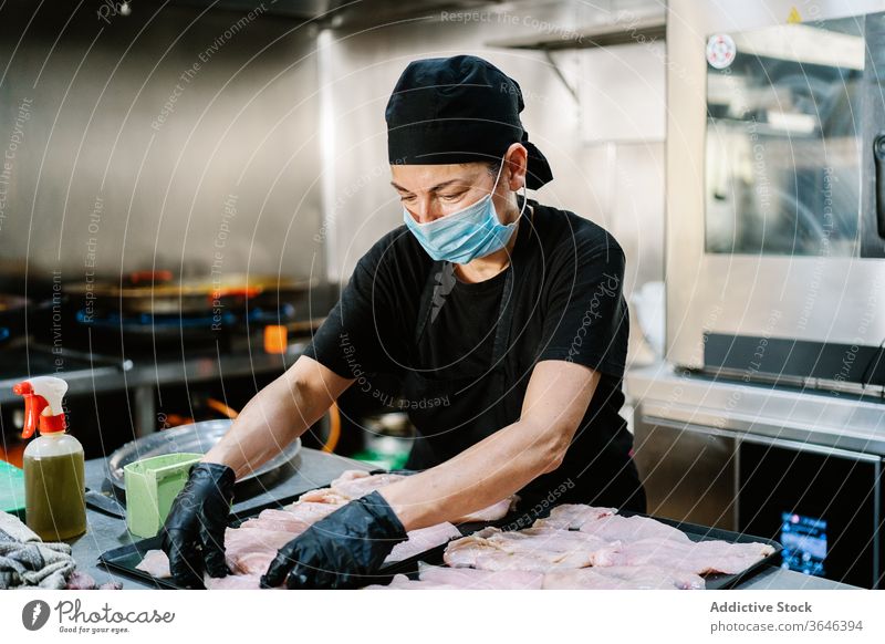 Fokussierte Köchin mit Gesichtsmaske, die Fleisch zubereitet Küchenchef Frau Atemschutzgerät Tablett ernst Restaurant Coronavirus Bestandteil Lebensmittel Koch