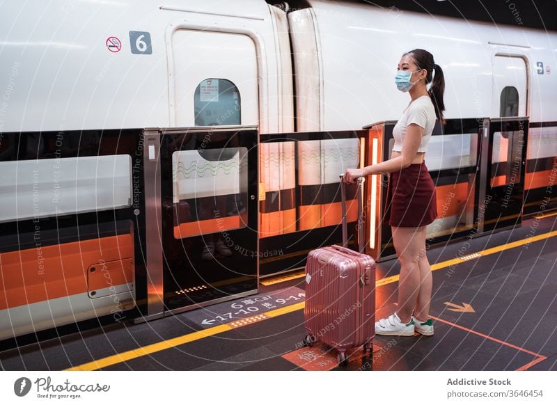 Asiatische Frau mit Beatmungsgerät wartet am Bahnhof auf das Einsteigen in den Zug Koffer Holzplatte reisen Podest Coronavirus Windstille Kabine Passagier
