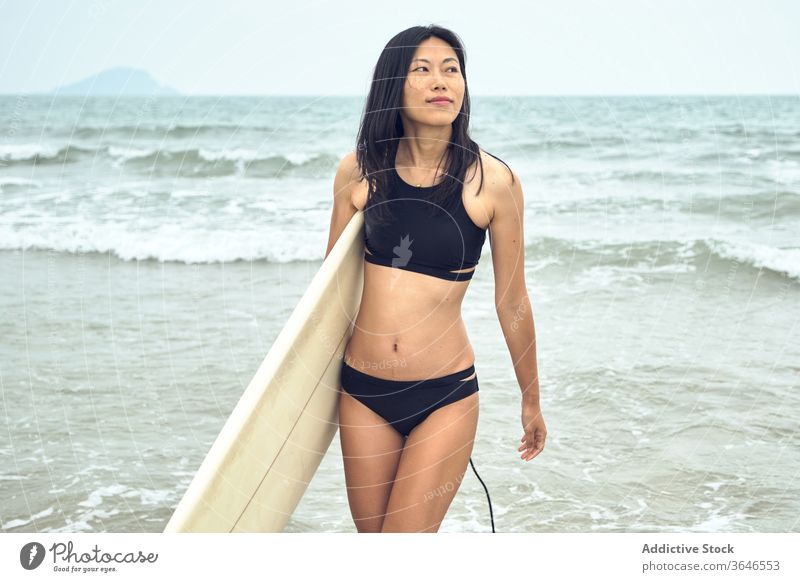 Zufriedene Surferin, die mit einem Surfbrett am Strand spazieren geht Frau Spaziergang sandig führen Inhalt MEER lässig Seeküste sorgenfrei Aktivität jung