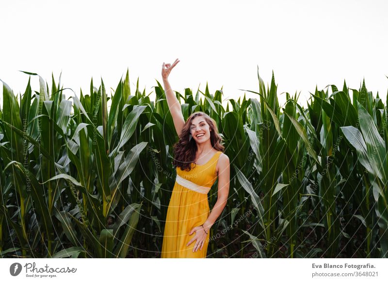 Porträt einer jungen schönen Frau in einem gelben Kleid, die in einem grünen Maisfeld steht. Sommerzeit und Lebensstil 1 v-Zeichen Schönheit sorgenfrei lässig