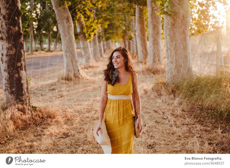 Porträt einer jungen schönen Frau in einem gelben Kleid, die an einem Pfad mit Bäumen entlang geht. Sommerzeit und Lebensstil Abenteuer Rücken Schönheit hell