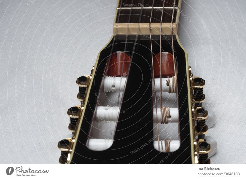 Ein schwarzer Gitarren Kopf mit den goldene Stimmwirbeln und die Seiten aus Kunststoff und Metall befestigt an den weißen Schrauben. Ein kleiner Teil des Griffbretts ist noch sichtbar.