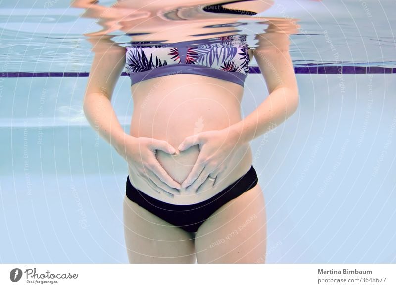 Schwangere Frau mit Babybauch, die mit ihren Händen ein Herz bildet, Unterwasserfangung unter Wasser Bauch Mutterschaft Schwangerschaft schwanger Pool