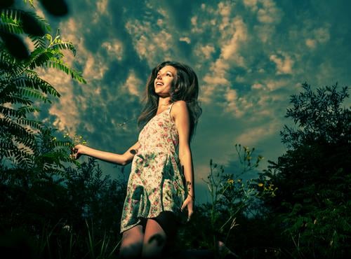 Ein fröhliches Mädchen tanzt im hohen Gras vor dem dramatischen Himmel. Hochsprung in Frühlingsfeldern. Sie ist in ein leichtes Sommerkleid gekleidet. Tanzen
