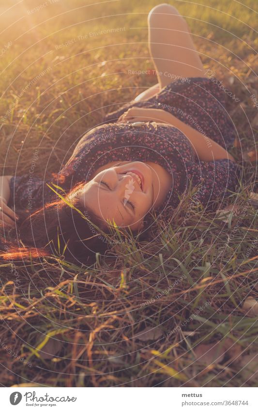 Glückliches Mädchen liegt im herbstlichen Gras und lacht im Gegenlicht des Sonnenuntergangs Aktivität Rückansicht nackte Beine Mitteilung gekreuzte Beine